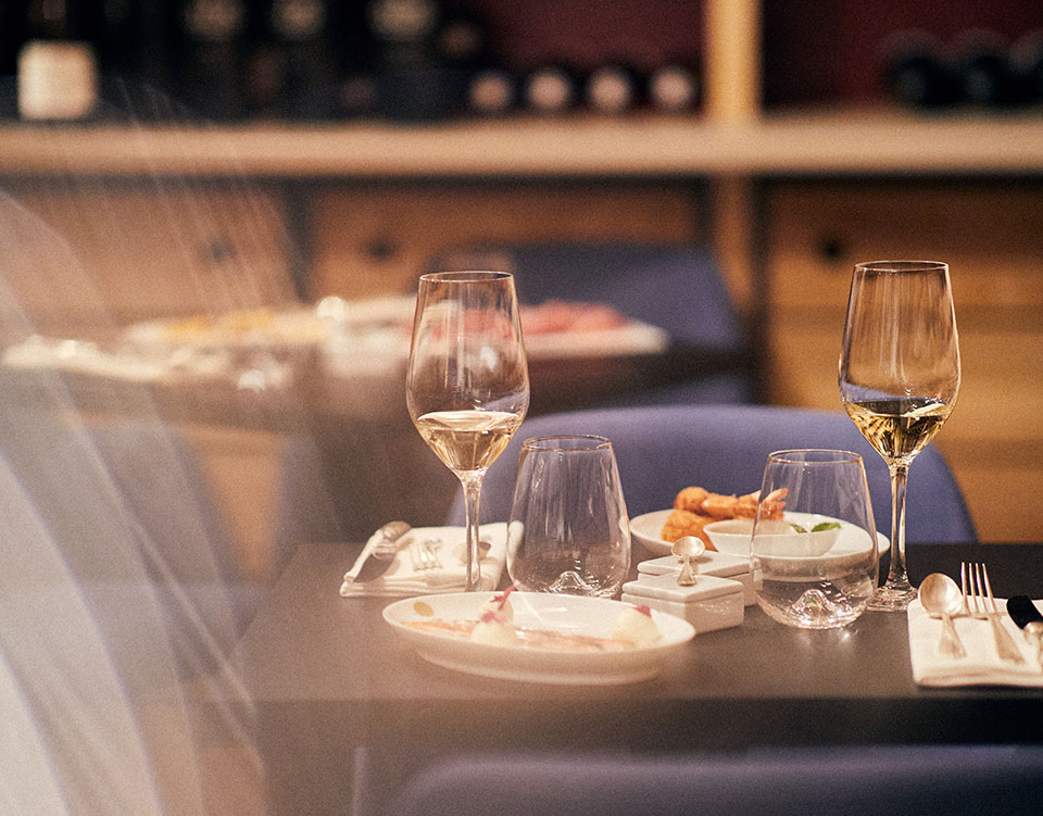 Photo d'une table pour deux de la salle du restaurant du 5 Wine Bar situé dans une cave sous le bar : 2 verres de vin blanc et 2 assiettes avec menu gastronomique